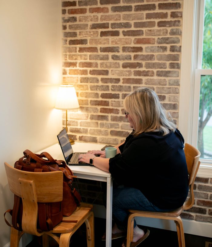 A blonde woman sits at a table working on her laptop.